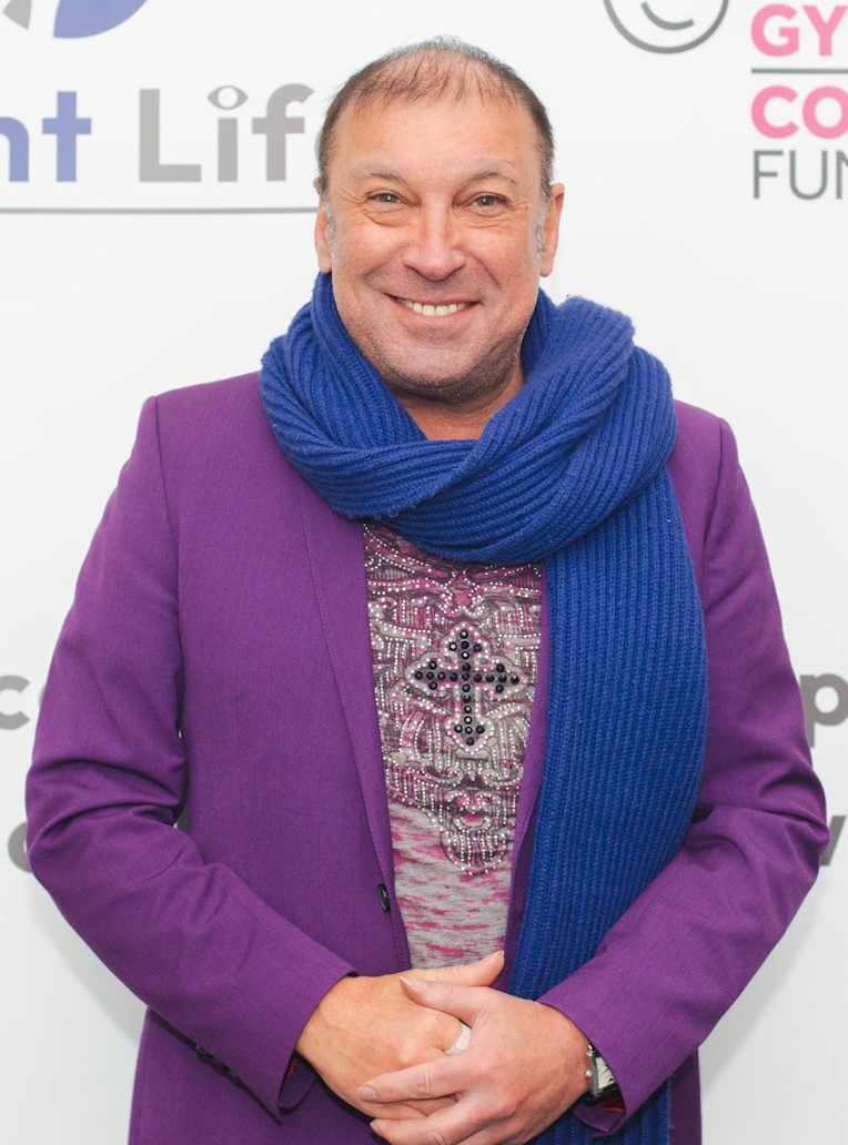 Head and shoulders portrait of Ceri Dupree standing in front of a Sight Life banner. He's wearing a purple jacket and blue scarf around his neck. He's smiling warmly to camera.