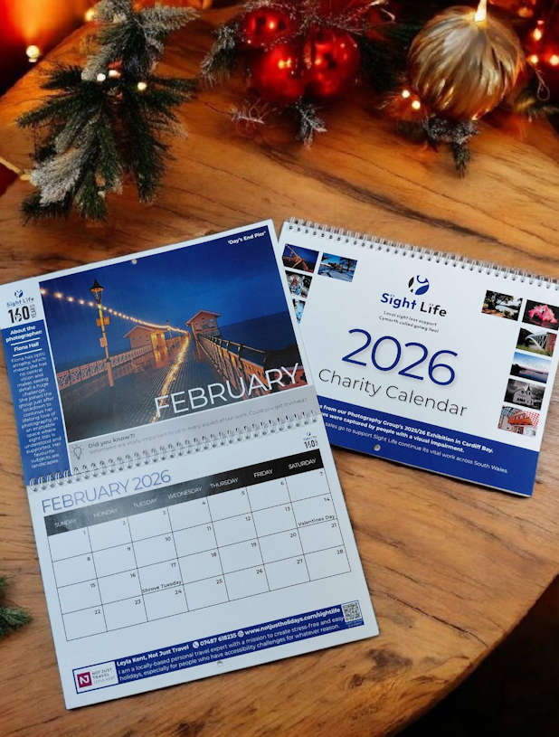 A photo of 2 of the Charity calendars - one open and one folded showing the front cover, on a wooden table. There is some Christmas greenery across the top of the image.