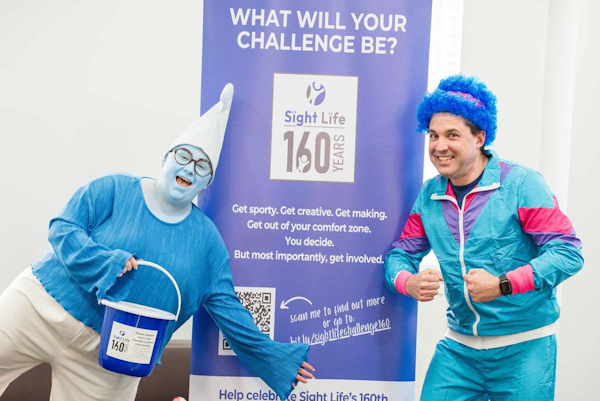 Picture of two of Robertsons staff dressed up in blue in front of a Sight Life Challenge 160 banner.