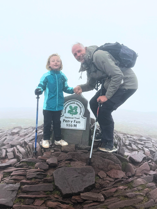 Picture of Aria and her father stood in front of the Pen Y Fan summit plaque.