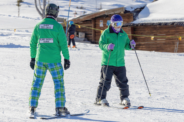 Picture of VI Skier on the slopes with Blind Skiers Guide stood to their side.
