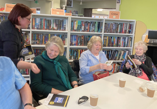 Picture of Sight Life members sat around a table at Radyr hub with a row of bookshelves in the background.